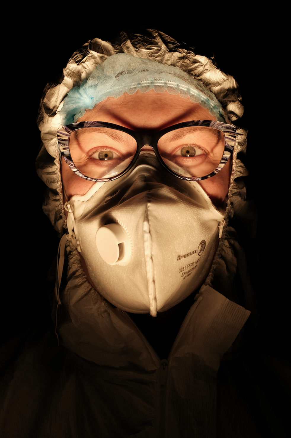A female nurse wearing a face mask with a dark background behind her