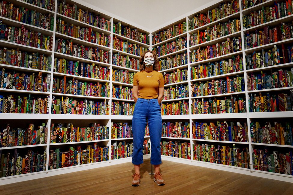 A member of staff wearing a face mask stands before a portion of an artwork