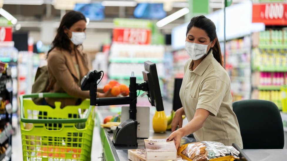 A woman shopping for food wears a face mask, as does the cashier