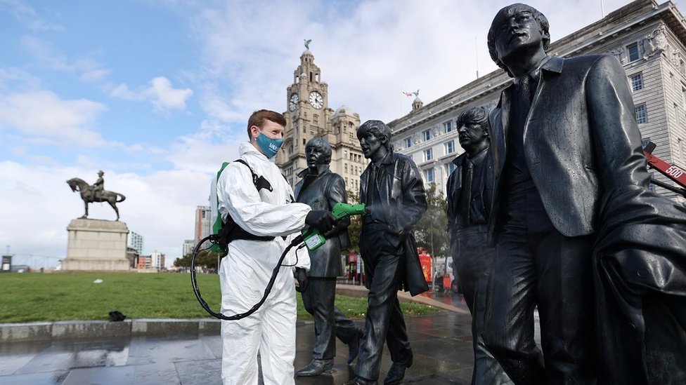 A man wearing a face covering cleaning statues of the Beatles