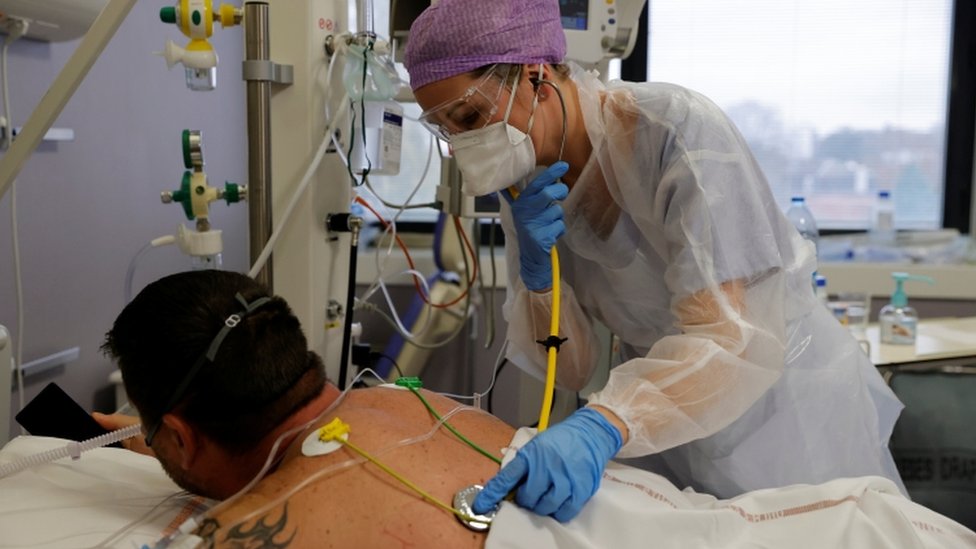 A doctor wearing a protective suit and a face mask, examines a patient in the intensive care unit in France