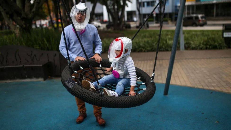 Father and son playing at a swing, wearing full face 'helmet-masks', and the little child has been dressed up so he looks like an astronaut