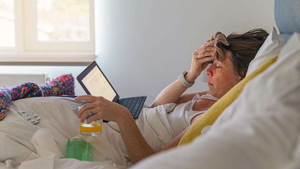 A woman in bed looking unwell watching a laptop