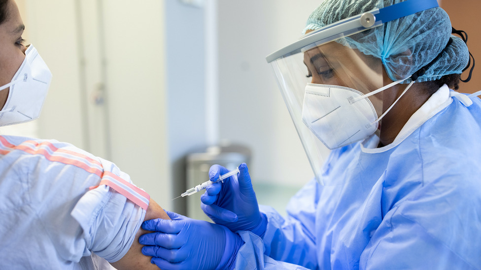 Someone in protective clothing giving another person an injection