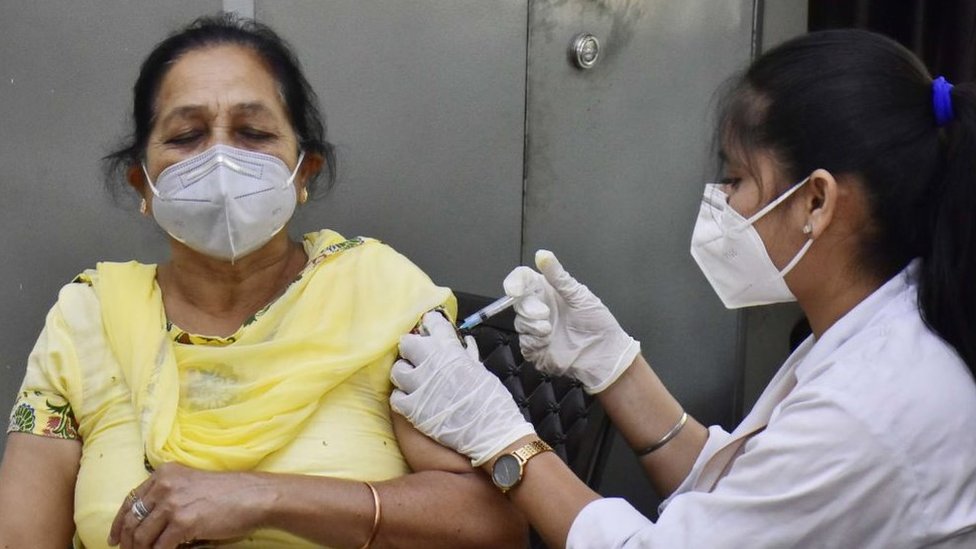 An older woman in a face mask receiving a vaccination from a younger woman in a face mask