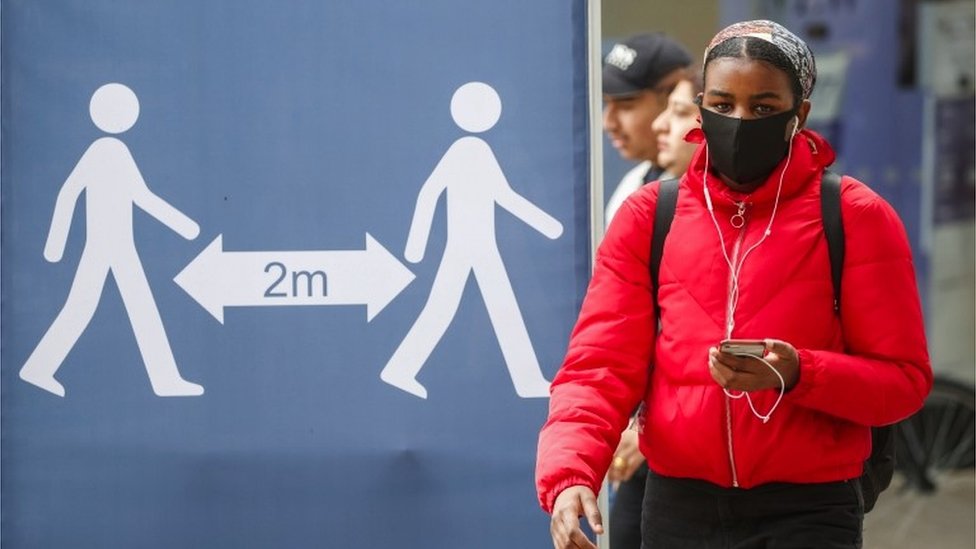 A woman walks past a sign calling for social distancing