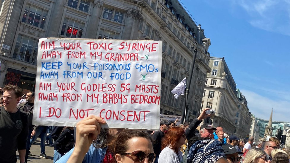 Woman with a sign listing conspiracy theories about toxic syringes and 5G phone technology