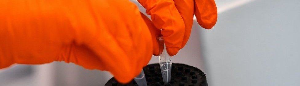 A lab worker shaking a vial that contains a sample of coronavirus