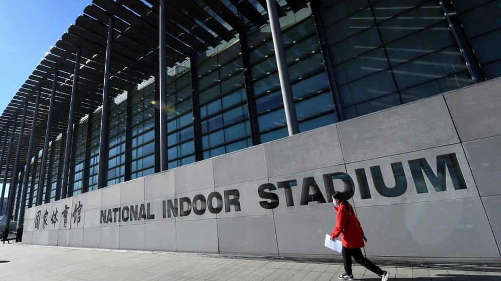 A woman walks past the National Indoor Stadium before an ice hockey match, part of a 2022 Beijing Winter Olympic Games test event, in Beijing on November 10, 2021.