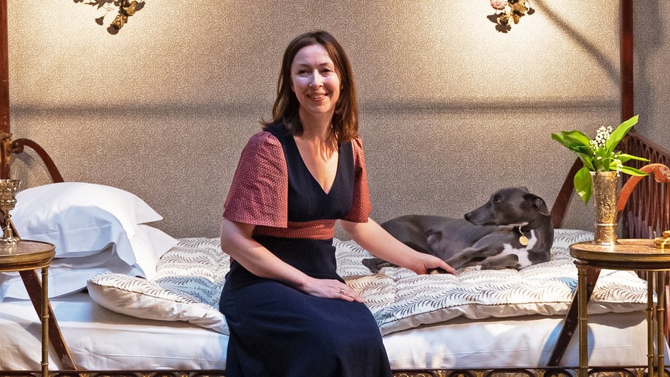 Lulu Lytle sitting on a bed, holding a greyhound's paw