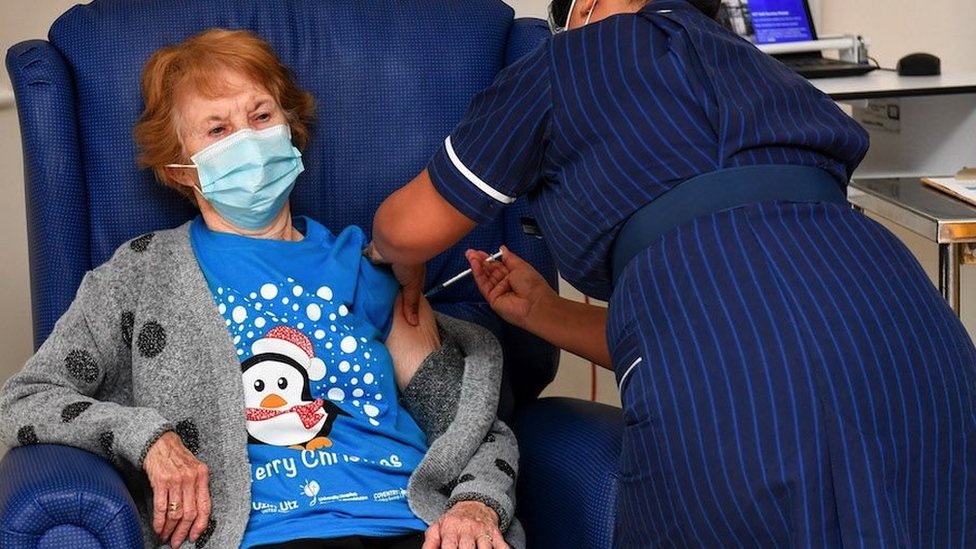Margaret Kenan prva je u Ujedinjenom Kraljevstvu koja je primila vakcinu Fajzer/Biontek kovid-19 u Univerzitetskoj bolnici u Koventriju, u dobi od 90 godina, koju je dala medicinska sestra Mai Parsons, 8. decembra 2020. u Koventriju, Ujedinjeno Kraljevstvo.